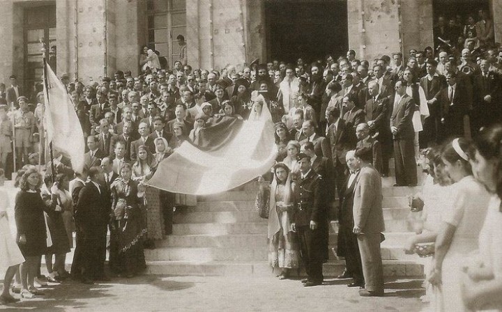 Ρόδος, 31 Μαρτίου 1947. Δώδεκα νέες με τοπικές ενδυμασίες που συμβολίζουν τα δώδεκα ελεύθερα νησιά σηκώνουν στα χέρια την ελληνική σημαία. Οι Αρχές και πλήθος κόσμου περιμένουν να ξεκινήσει η πομπή από το Δημαρχείο προς το κτήριο της Διοίκησης Δωδεκανήσου.(Αρχείο Συμεών Δοντά)